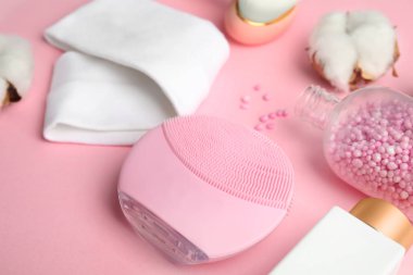 Pembe arka planda yüz temizleme fırçası ve kozmetik ürünleri