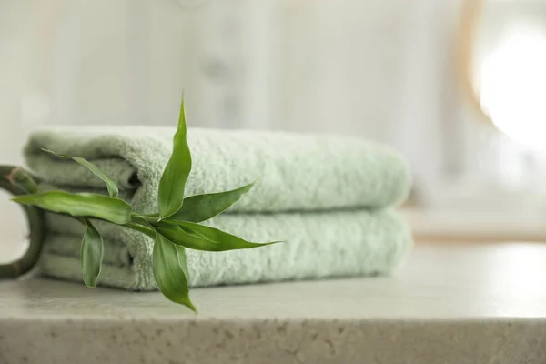 Stack of clean towels and bamboo sprout on table in bathroom — Stock Photo, Image