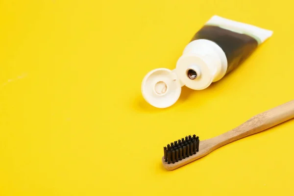 Escova de dentes feita de bambu e pasta de carvão vegetal no fundo amarelo — Fotografia de Stock