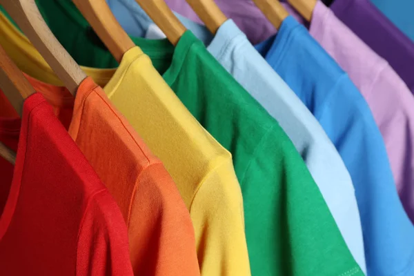 Яркая одежда на деревянных вешалках, крупный план. Радужные цвета — стоковое фото