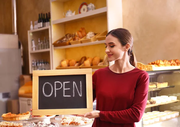 Žena majitel podniku držení otevřené znamení v pekařství — Stock fotografie