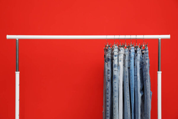 Rack with stylish jeans on red background