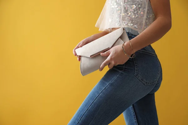 Vrouw in jeans met clutch tas op gele achtergrond, close-up — Stockfoto