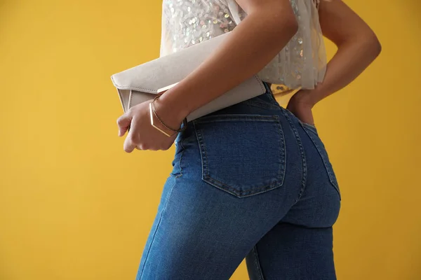 Mulher de jeans com bolsa de embreagem no fundo amarelo, close-up — Fotografia de Stock