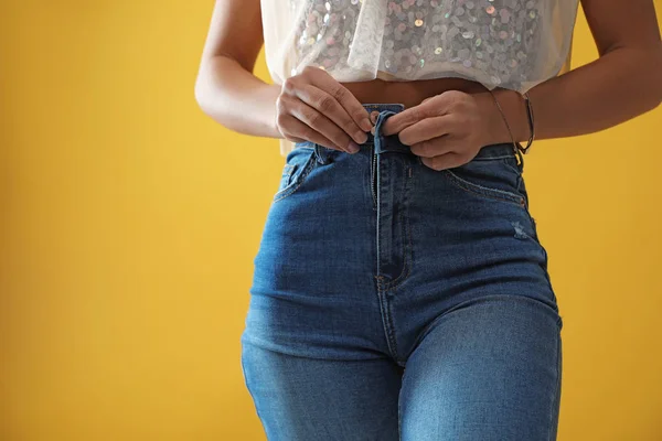 Woman unbuttoning jeans on yellow background, closeup — ストック写真