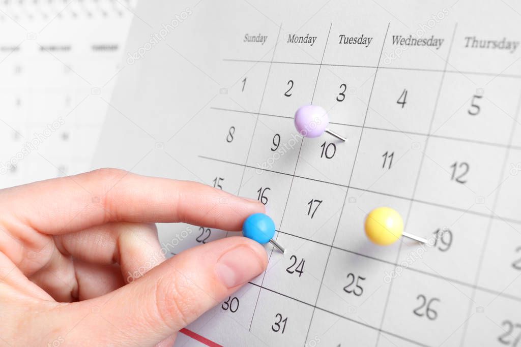 Woman marking date in calendar with drawing pin, closeup