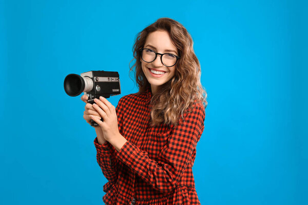 Beautiful young woman with vintage video camera on light blue ba