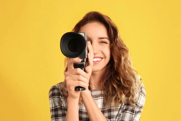 Mooie jonge vrouw met vintage videocamera op gele backgr — Stockfoto