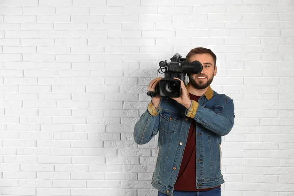Operador com câmera de vídeo profissional perto da parede de tijolo branco, s — Fotografia de Stock