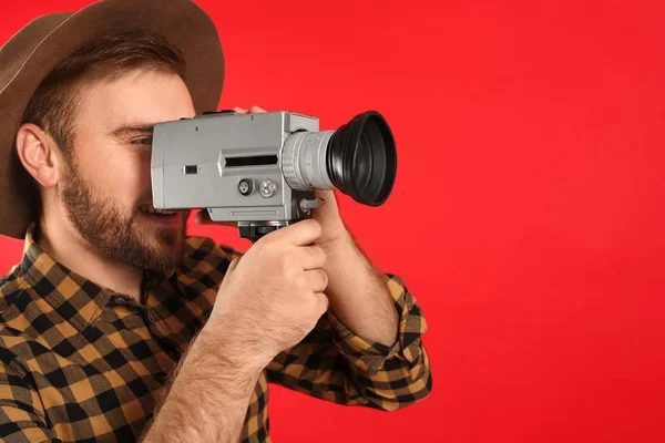 Young man with vintage video camera on red background