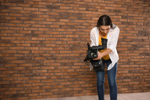 Operador com câmera de vídeo profissional perto da parede de tijolo, espaço f — Fotografia de Stock