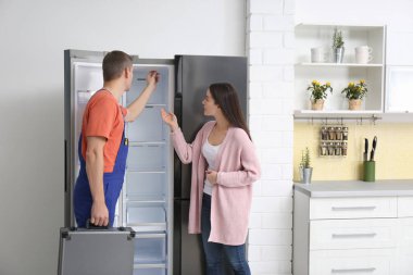 Erkek teknisyen müşteriyle mutfakta buzdolabının yanında konuşuyor.