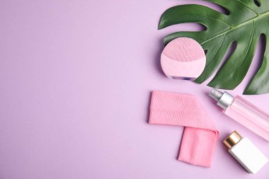 Menekşe arkaplan üzerinde yüz temizleyici fırça ile düz kompozisyon, metin için boşluk. Kozmetik aksesuar