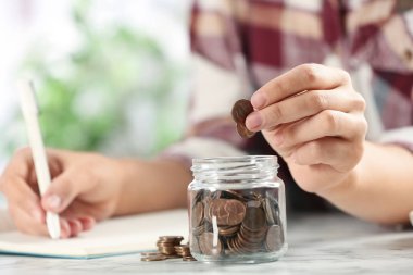 Kadın, beyaz mermer masada cam kavanoza para koyuyor.