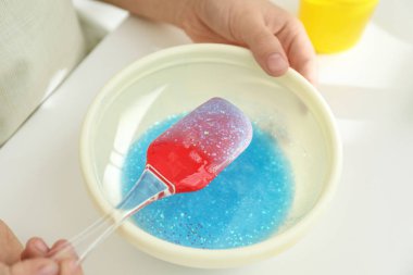 Küçük kız masadaki silikon spatulayla malzemeleri karıştırıyor, yakın plan. Çamur oyuncağı