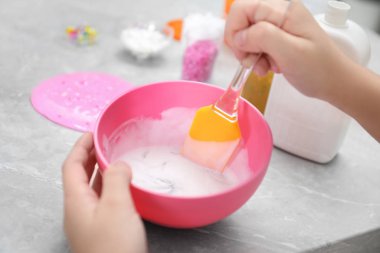 Küçük kız masadaki silikon spatulayla malzemeleri karıştırıyor, yakın plan. Çamur oyuncağı
