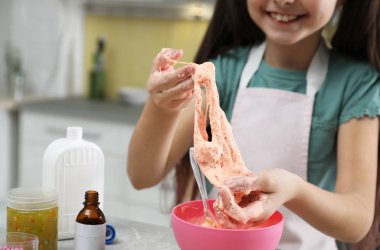 Küçük kız mutfaktaki masada Diy Slime oyuncağını yoğuruyor.