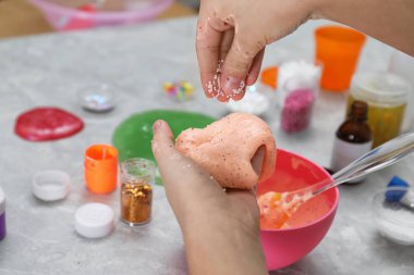 Little girl adding decorative balls to homemade slime toy at table, closeup clipart