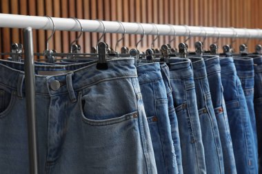 Ahşap arka planda farklı kot pantolonları olan raflar, yakın plan