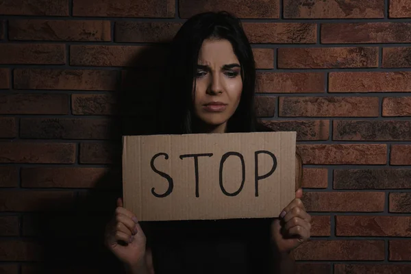 Abused young woman with sign STOP near brick wall. Domestic violence concept