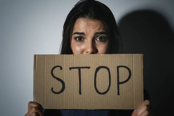 Κακοποιημένη νεαρή γυναίκα με πινακίδα Στάση κοντά σε λευκό τοίχο. Ενδοοικογενειακή βιόλη — Φωτογραφία Αρχείου