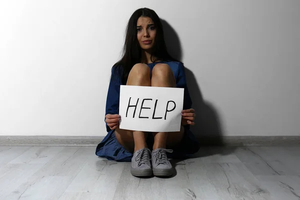 Κακοποιημένη νεαρή γυναίκα με πινακίδα Βοήθεια κοντά σε λευκό τοίχο. Ενδοοικογενειακή βιόλη — Φωτογραφία Αρχείου