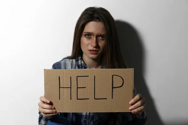 Κακοποιημένη νεαρή γυναίκα με πινακίδα Βοήθεια κοντά σε λευκό τοίχο. Ενδοοικογενειακή βιόλη — Φωτογραφία Αρχείου