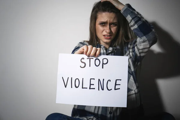 Mujer joven llorona con signo PARAR LA VIOLENCIA cerca de la pared blanca — Foto de Stock