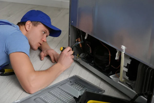 Técnico masculino con destornillador reparando refrigerador en interiores — Foto de Stock