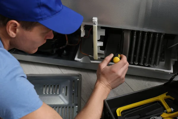 Técnico masculino con destornillador reparando refrigerador en interiores —  Fotos de Stock