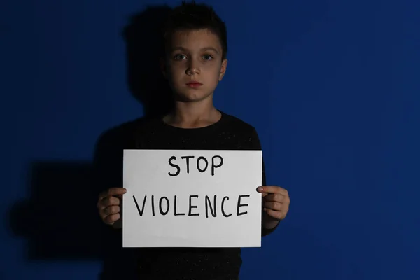 Niño abusado con signo PARAR LA VIOLENCIA cerca de la pared azul —  Fotos de Stock