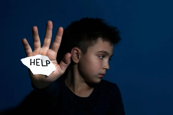 Abused little boy with sign HELP near blue wall, focus on hand. — Stock Photo, Image