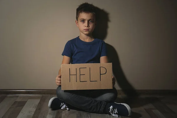 Abused little boy with sign HELP near beige wall. Domestic viole — Stock Photo, Image