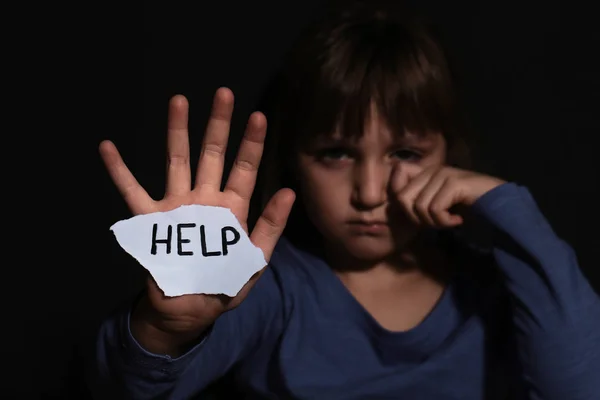 Síró kislány táblával Segítség a fekete fal közelében, összpontosítson a kézre — Stock Fotó