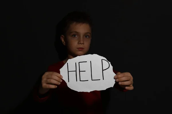 Abused little boy with sign HELP near black wall. Domestic viole — Stock Photo, Image