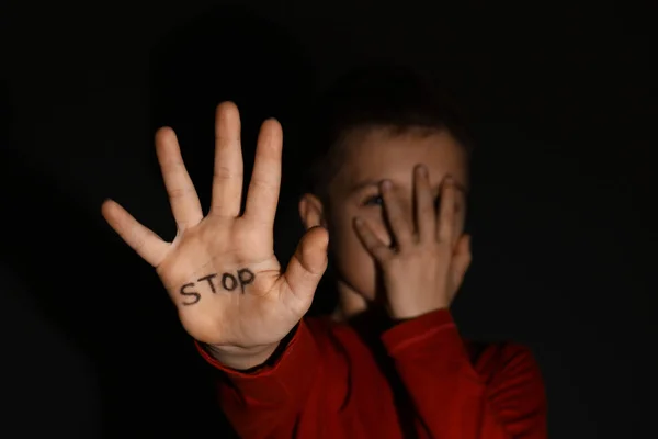 Niño abusado mostrando la palma de la mano con la palabra DETENER contra espalda negra — Foto de Stock