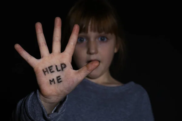 Abused little girl showing palm with phrase HELP ME on black bac