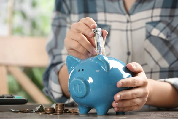 Vrouw zet geld in spaarvarken bank aan tafel, close-up — Stockfoto