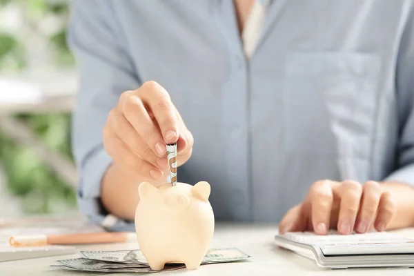 Woman putting money into piggy bank at table, closeup — Stock Photo, Image