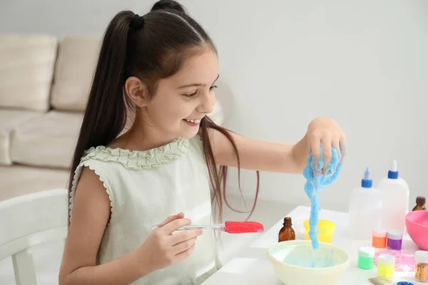 Милая маленькая девочка делает самодельную слизистую игрушку за столом в комнате — стоковое фото