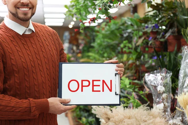 Male business owner holding OPEN sign in his flower shop, closeup