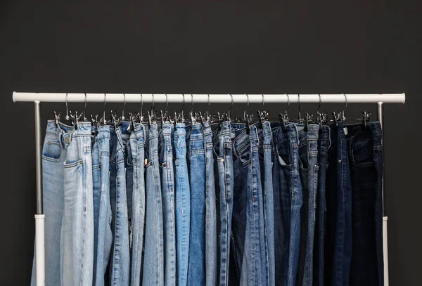 Стойка с различными джинсами на темно-сером фоне — стоковое фото