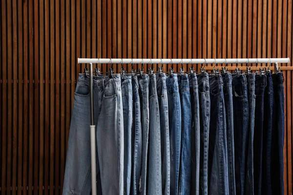 Rack with different jeans on wooden background — Stock Photo, Image