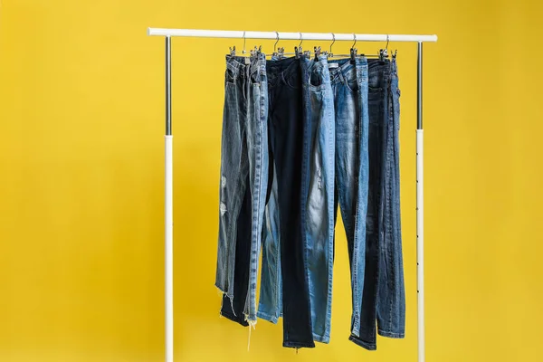 Bastidor con diferentes pantalones vaqueros sobre fondo amarillo — Foto de Stock