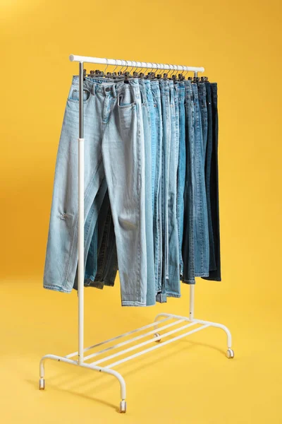 Cremalheira com jeans diferentes no fundo amarelo — Fotografia de Stock