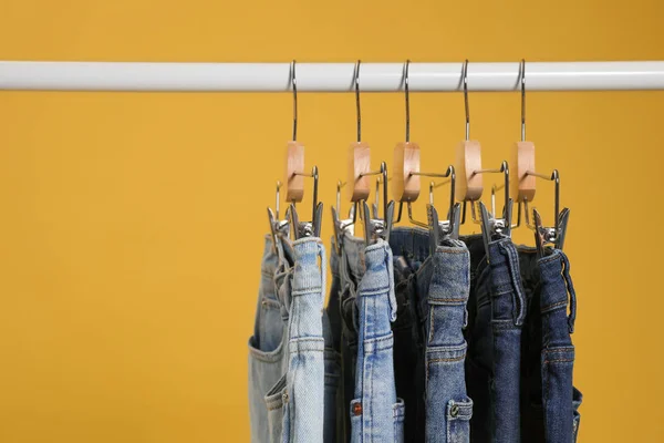 Rack with different jeans on yellow background — Stock Photo, Image