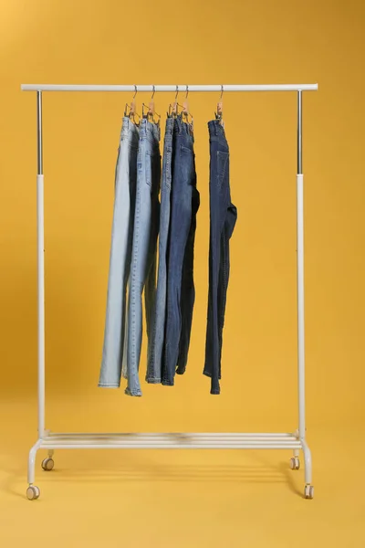 Scaffale con diversi jeans su sfondo giallo — Foto Stock