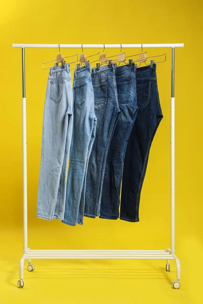 Ständer mit verschiedenen Jeans auf gelbem Hintergrund — Stockfoto