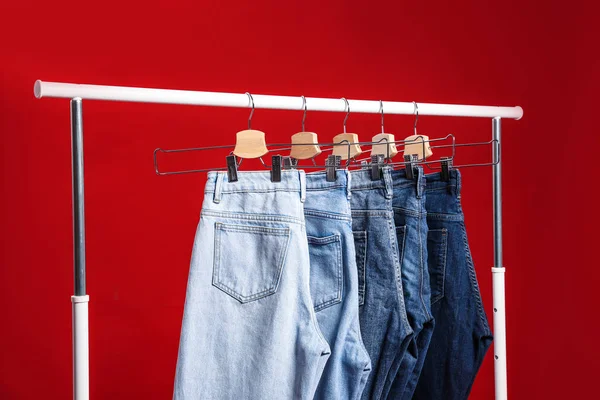 Bastidor con diferentes pantalones vaqueros sobre fondo rojo —  Fotos de Stock