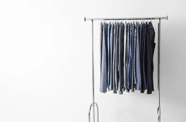 Rack met verschillende jeans in de buurt van lichte muur. Ruimte voor tekst — Stockfoto